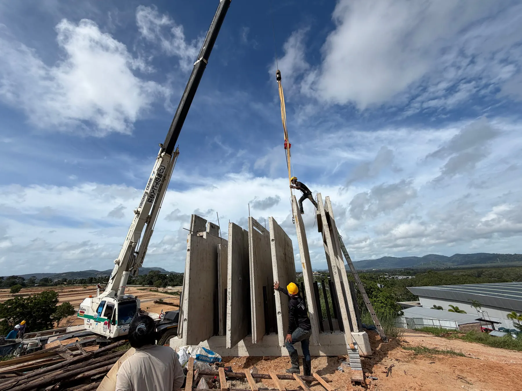 Precast wall panels going up against blue sky, workers + crane