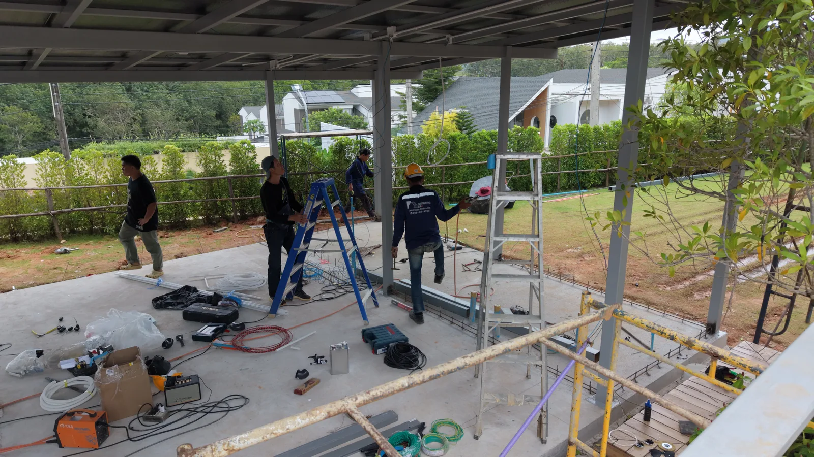 Project management: multiple in-house trades coordinated on site under a covered canopy at active build